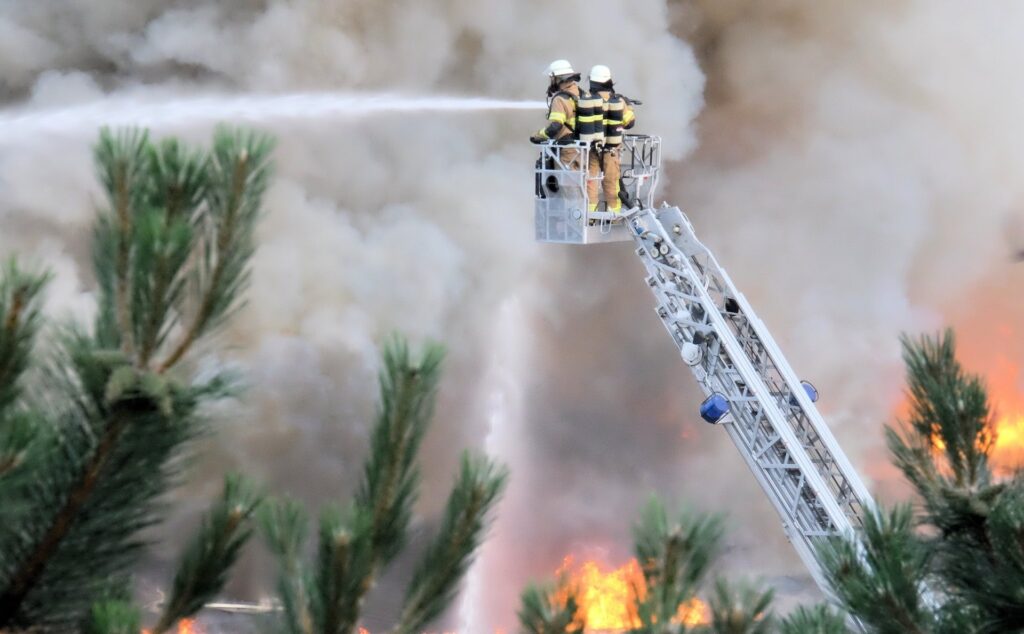 Firefighters up in the sky fighting fires with water above trees and smoke.